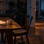 A dimly lit living room with an open book, half-finished cup of tea, an empty chair, and a partially open door, creating an unsettling feeling that someone has just left.